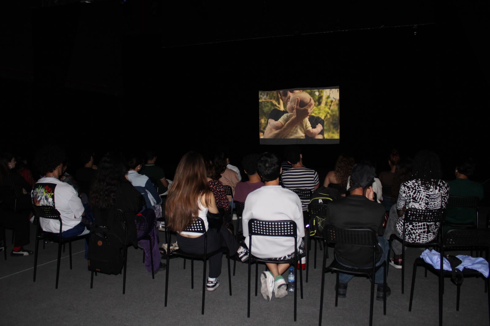 An audience seated in a dark studio watches a film screening